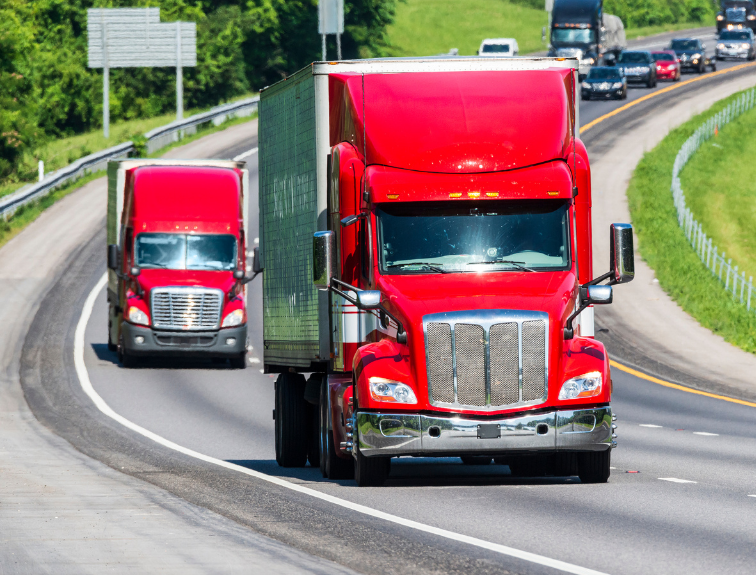 image of two red semi trucks driving down interstate